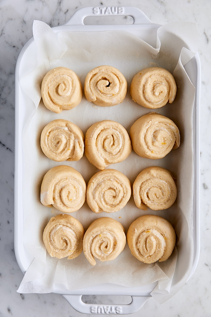Unbaked lemon rolls in ceramic parchment-lined baking dish