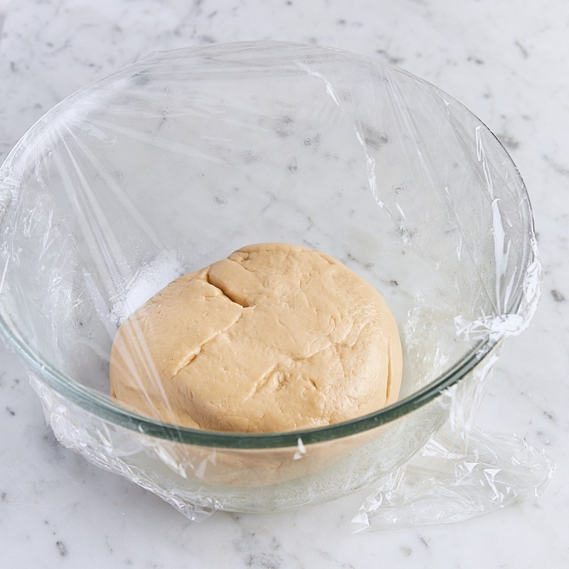 Dough in glass mixing bowl covered with plastic wrap