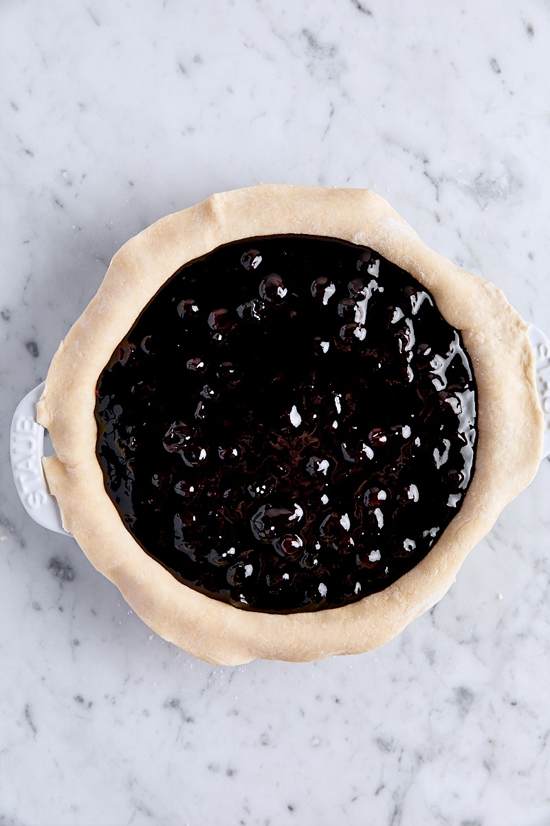 Blueberry filling spooned into pie dough in pie pan