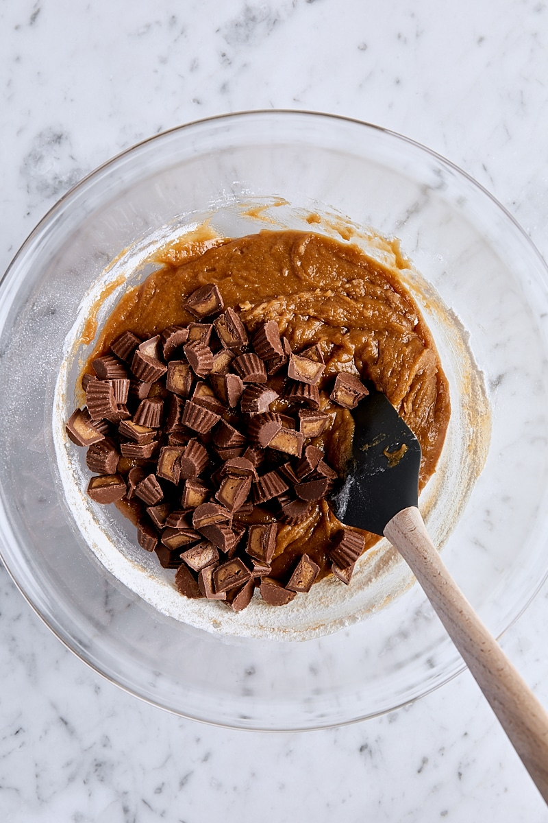 Mini peanut butter cups added to blondie batter in glass bowl