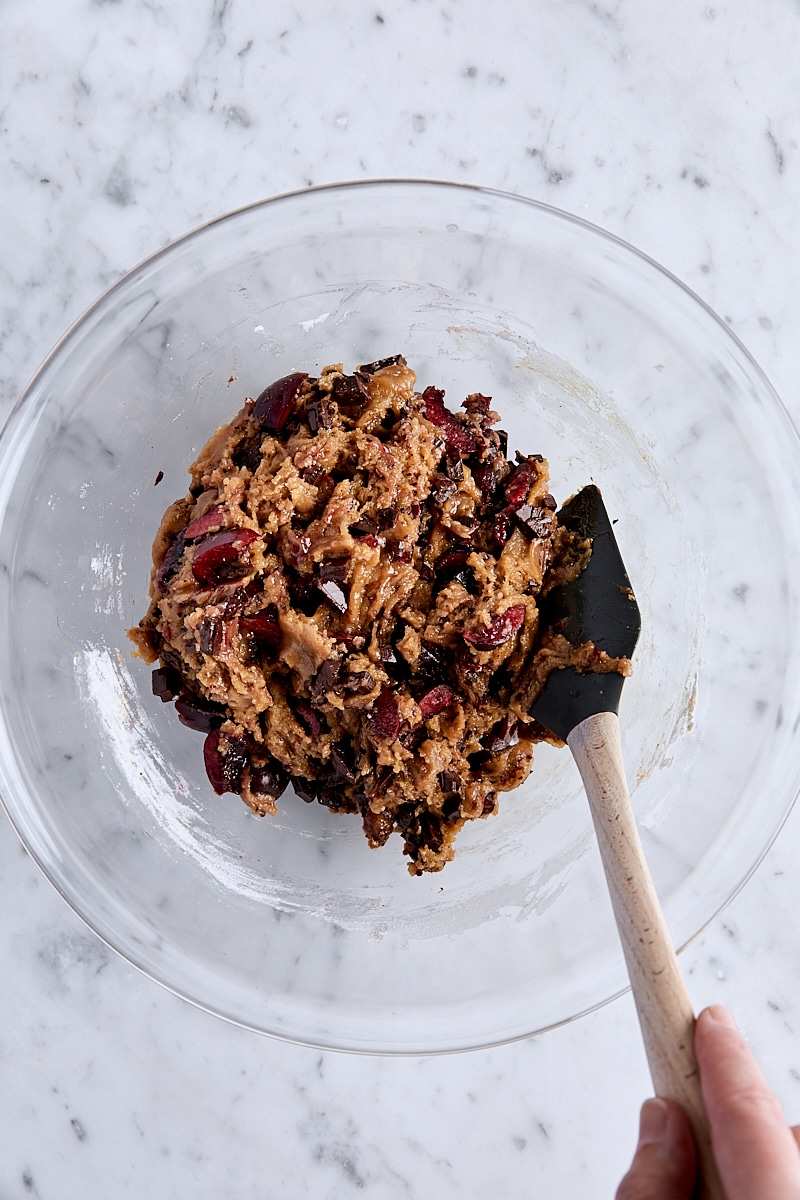 Mixed cherry chocolate blondie batter in glass bowl with spatula