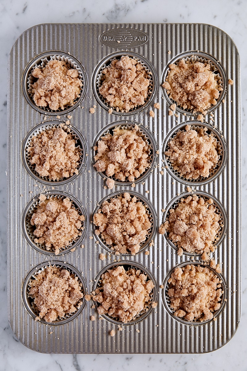 Coffee cake muffin batter scooped into muffin tin and sprinkled with crumb topping