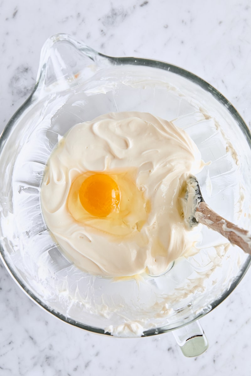 Egg added to cheesecake batter in glass mixing bowl