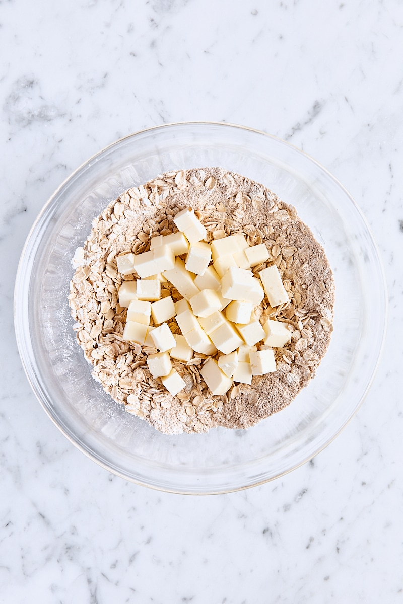 Cubed butter added to oatmeal mixture in glass bowl