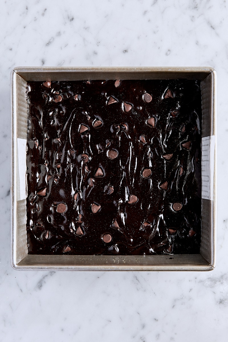 Cocoa brownie batter spread into parchment-lined square baking pan